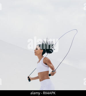 Cropped shot of a female athlete in fitness wear working out with a skipping rope. Side view of a fitness woman doing fitness training. Stock Photo
