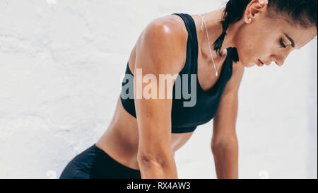 Portrait of a fitness woman relaxing during workout looking down. Cropped shot of a woman in fitness wear taking a break from workout and relaxing. Stock Photo