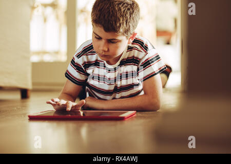 Boy using a tablet pc lying on floor at home. Kid playing games on a tablet computer. Stock Photo