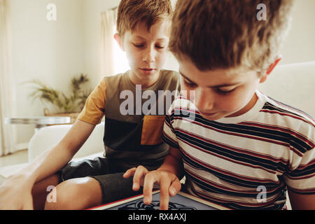 Boys spending time learning on a tablet pc. Boy playing game on a tablet pc while his friend looks on. Stock Photo