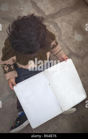 High angle view of Cute 2 year little Indian Asian baby girl kid with blank book while sitting on the floor. Stock Photo