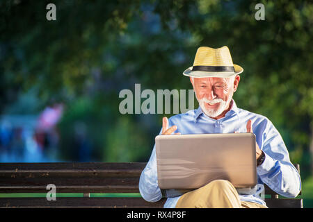 Senior man using laptop computer at rest in the park outdoors Stock Photo