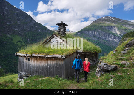 Kagefla - historic mountain farms on the mountainsides along the Geirangerfjorden fjord. Tourist attraction of Norway. A pair of travelers visiting tr Stock Photo