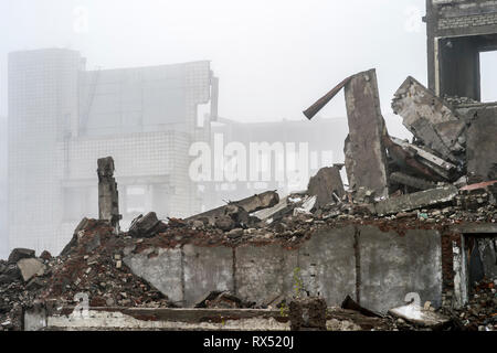 The remains of the destroyed building in the form of piles and a blockage of a pile of stones on the background of a high destroyed structure in a fog Stock Photo