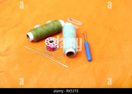 Photo of colored sewing thread, needle, bobbin, button, safety pin and needle ripper. Isolated on the yellow background. Stock Photo