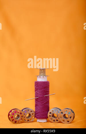 Photo of one pink sewing thread and bobbins. Isolated on the yellow background.