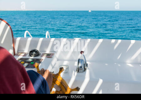 People at the helm of a white yacht. A man Arab controls the yacht. Foot on the yacht steering wheel. Stock Photo