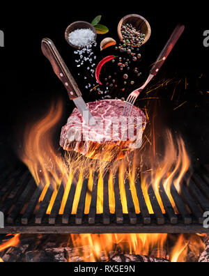 Raw Steak ribeye cooking. Conceptual picture. Steak with spices and cutlery under burning grill grate. Stock Photo