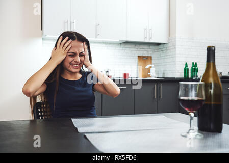 Depressed, divorced woman sitting alone in kitchen at home in the kitchen. She is going to drink a glass of red wine because of problems at work and t Stock Photo