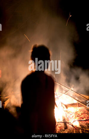 A blurred silhouette of a woman is backlight by an outdoor glowing bonfire at night, Cevennes, France Stock Photo