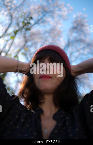 low angle close up of beautiful french woman with woolly hat and her hands behind her head, looking relaxed and happy about the advent of Spring Stock Photo