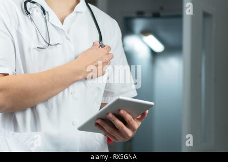 Bright close up of male doctor in uniform holding stethoscope and using computer tablet in hospital. Medical concept with copy space Stock Photo