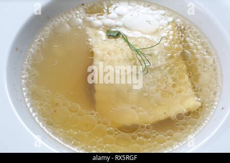 Minimalistic serving of food, white transparent chicken broth in a plate of rice, cheese and dumplings, decorated with pea germ Stock Photo