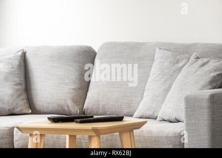 Interior of modern sunny living room with remote controls for television set on a wooden table. Gray sofa in the background. Stock Photo