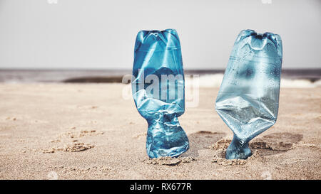 Two plastic bottles stuck in sand on a beach, selective focus, color toning applied. Stock Photo
