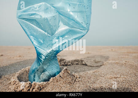 Close up picture of a plastic bottle stuck in sand on a beach, selective focus, color toning applied.