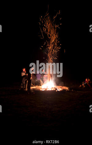 a crowd of people standing around a large bonfire which lights them up on a dark Winter’s night in the Cevennnes, France Stock Photo