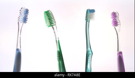Four colorful transparent tooth brushes on pink and blue gradient background. Horizontal composition. Stock Photo