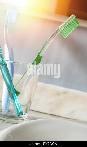 Toothbrushes in a glass cup on a sink. Vertical composition. Front view. Stock Photo