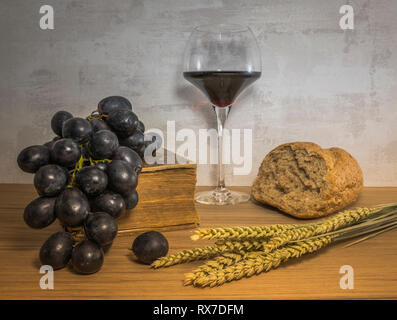 A wheat bread and shock of wheat with red grapes and glas of red wine and bible as easter background Stock Photo