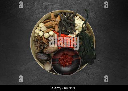 Various spices in natural bamboo bowl on black stone background. Assortment of dried spices: Saffron, black and red chilli, Lemongrass, Nutmeg, Cinnam Stock Photo