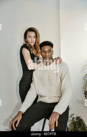 a good looking and young couple poses with next to each other and look at the camera she is white he is black they have serious faces