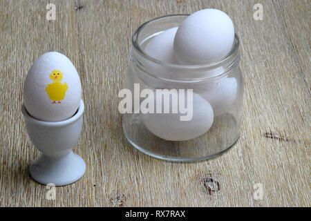Eggs in glass bowl and boiled egg with a yellow Easter chicken painted on it Stock Photo
