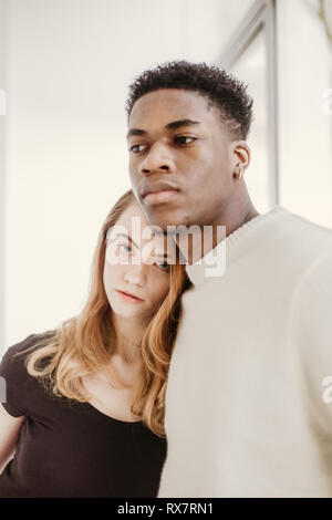 a good looking and young couple poses with next to each other and look at the camera she is white he is black they have serious faces