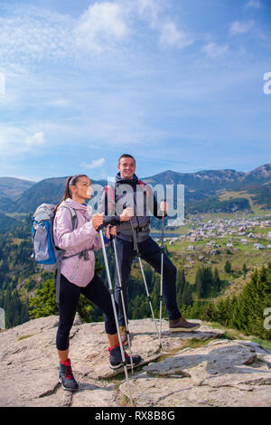 Hikers with backpacks relaxing on top of a mountain and enjoying the view of valley Stock Photo