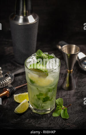 Mojito cocktail in glass with limes and bartending tools lying near Stock Photo