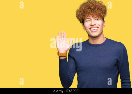 Young handsome man with afro hair Waiving saying hello happy and smiling, friendly welcome gesture Stock Photo