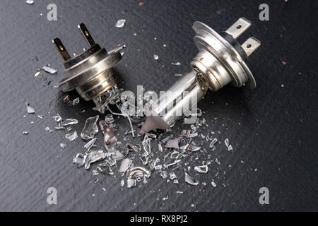 Broken bulb for the car headlight. Spilled glass and broken filament on the workshop table. Dark background. Stock Photo