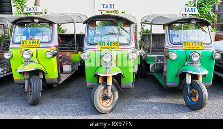 Bangkok, Thailand: Close-up panorama view of three isolated green colored Tuk-Tuk vehicles parking in front of a white wall without persons Stock Photo