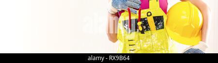 Cropped horizontal image female construction worker wearing yellow coverall holding protective hardhat posing over beige white background copy space f Stock Photo