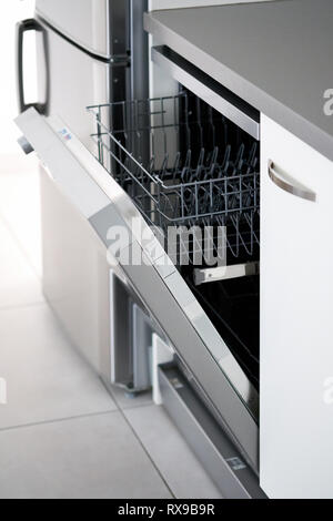 Side close up view open door of new clean empty dishwasher near fridge, mechanical device for cleaning dishware and cutlery automatically, concept mod Stock Photo