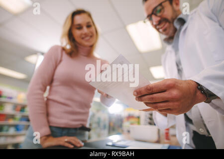 Male pharmacist helping female customer at pharmacy.  Chemist explaining a prescription to customer, Focus on prescription. Stock Photo