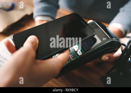 Customer paying bill through smartphone using NFC technology in pharmacy. Closeup of female hand holding her mobile phone over a card reader machine f Stock Photo