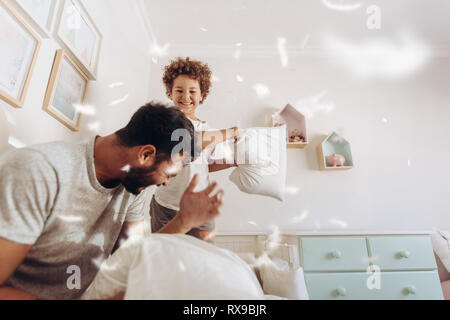 Happy boy pillow fighting with his father at home. Father and son having a  pillow fight on bed with feathers flying around. Stock Photo
