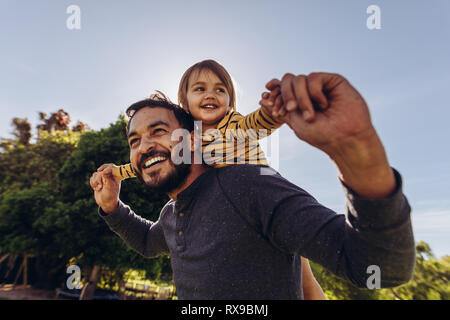 Close up of a man carrying his child on his back outdoors. Happy father walking outdoors with his kid on his back. Stock Photo