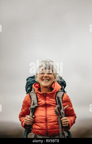 Senior woman hiker carrying a backpack trekking on a cloudy day. Happy woman on a vacation enjoying hiking. Stock Photo