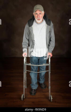 Vertical shot of elderly man walking with the aid of a walker across a wooden floor.  Brown background. Stock Photo