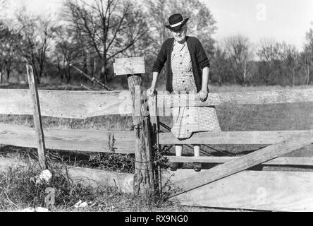 Horizontal black and white picture of an old lady climbing a fence with her fishing poles in the early 1900s.      Scanned old family photo. May conta Stock Photo
