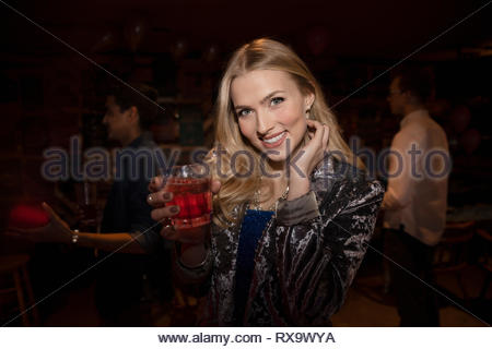 Portrait smiling young woman drinking cocktail in nightclub