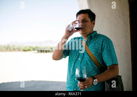Mature man drinking red wine while standing in corridor during sunny day Stock Photo