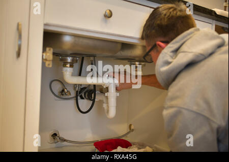 Side view of man adjusting pipes in kitchen at home Stock Photo