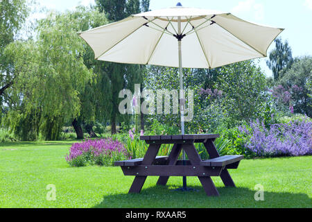 Relaxing setting in a pub garden with umbrella sitting bench next to flowers in bloom, willow trees, al fresco dining in an English countryside on a s