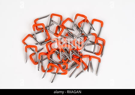Pile of Orange PVC Insulated Electrical Wire Safety Staples on white background. Staples are used to hold cable in place. Stock Photo