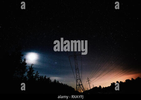 Low angle view of silhouette electricity pylons against star field at night Stock Photo