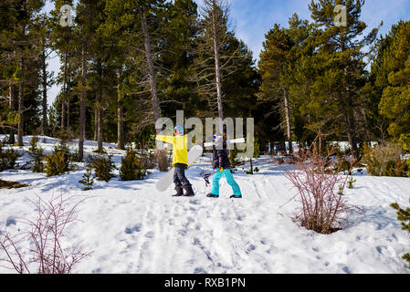 Side view of couple with snowboards walking on snow covered field in forest Stock Photo