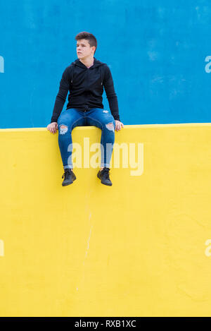 Confident man looking away while sitting on yellow retaining wall in city Stock Photo